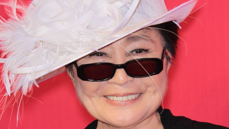 Yoko Ono lächelt mit Sonnenbrille und Federhut